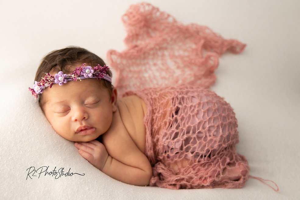 Foto de bebe menina envolta no wrap rosa deitada no puff