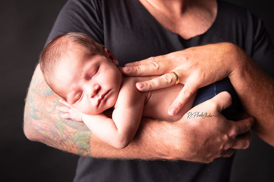 Foto de bebe menino aconchegado nos braços tatuados do pai