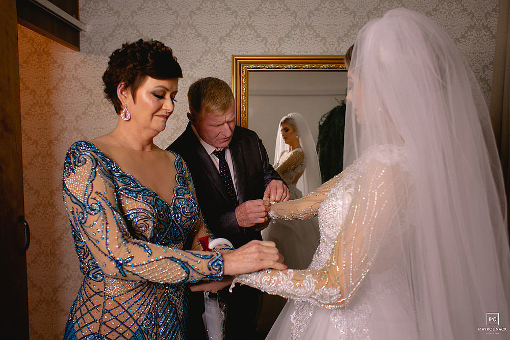 pai e mãe ajudando noiva a fechar vestido