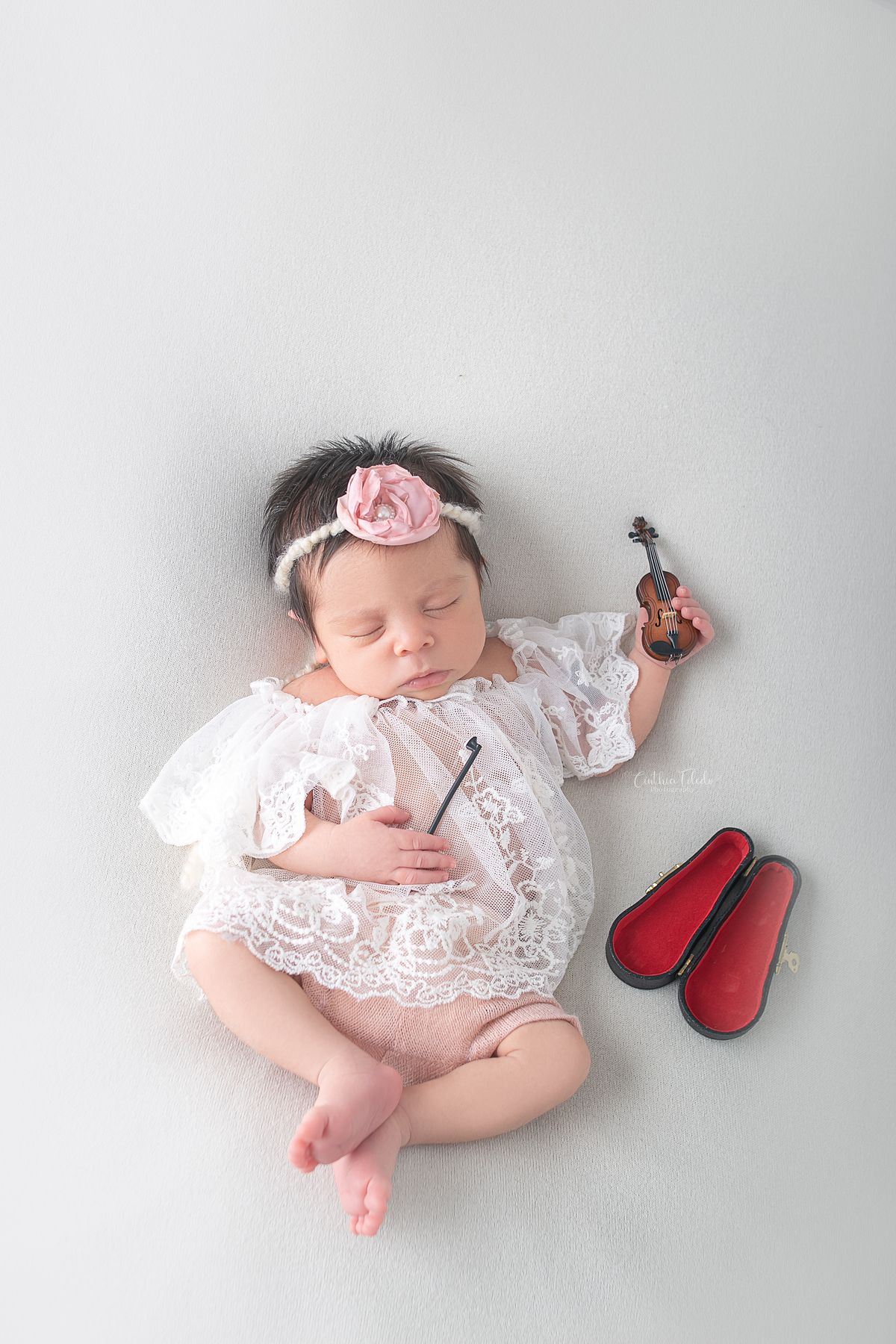 Ensaio fotográfico de Newborn / recém-nascido realizado em home-studio, localizado em Malden-MA, fotografado pela fotógrafa Cinthia Toledo Photography/fotografia. foto newborn com bebe dormindo no puff de barriga para cima segurando mini violino.