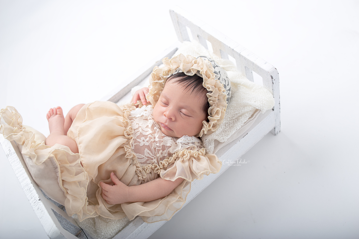 Ensaio fotográfico de Newborn / recém-nascido realizado em home-studio, localizado em Malden-MA, fotografado pela fotógrafa Cinthia Toledo Photography/fotografia. foto newborn na caminha de barriga para cima com vestido e fundo branco.