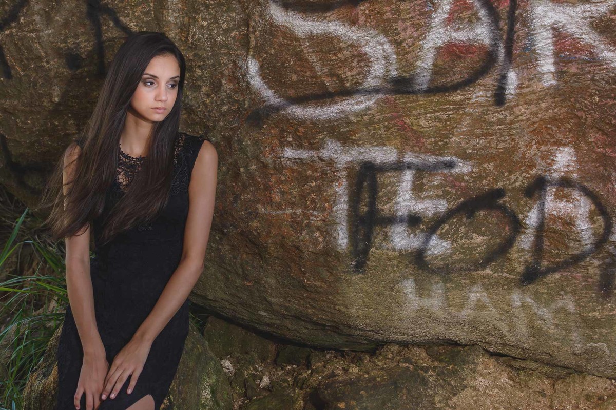 Fotografia da debutante encostada em uma pedra com grafite no Morro de Paranambuco em Itanhaém - ensaio de 15 anos - Cia P&B - Fotografia