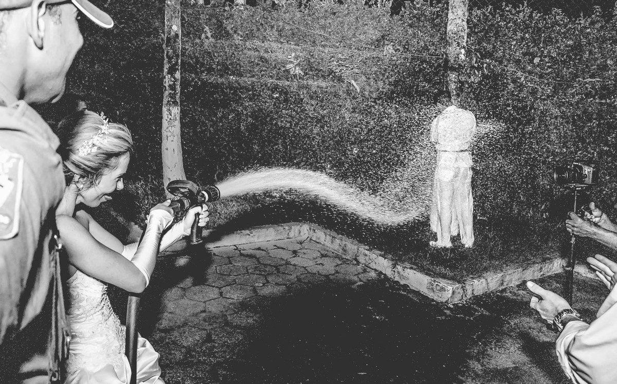 Fotografia de brincadeira dos noivos com a mangueira de bombeiros durante a festa de casamento no Iate Clube em Praia Grande - Cia P&B - Fotografia 