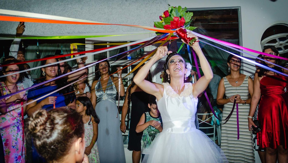 Fotografia da noiva cortando as fitas do buquê durante a festa de casamento no buffet Laranja em Mongaguá - Cia P&B - Fotografia