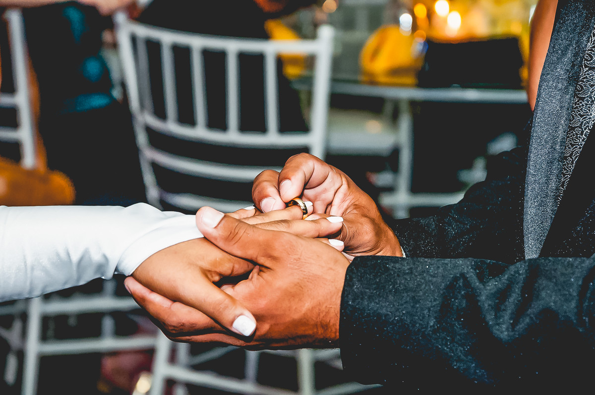 Fotografia do noivo colocando a aliança no dedo da noiva durante o casamento no buffet Espaço Free em Praia Grande - Cia P&B - Fotografia 