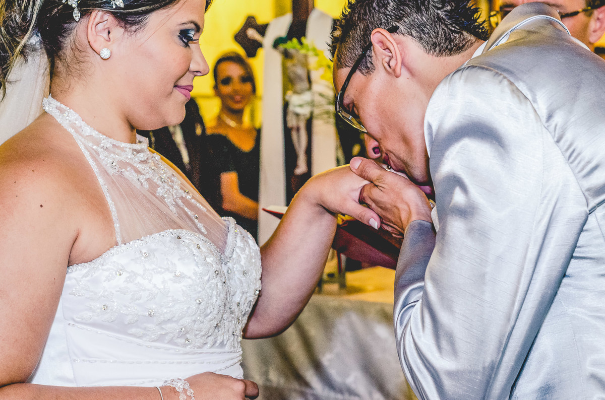 Fotografia do noivo beijando a aliança na mão da noiva durante o casamento na igreja Nossa Senhora Aparecida em Mongaguá - Cia P&B - Fotografia