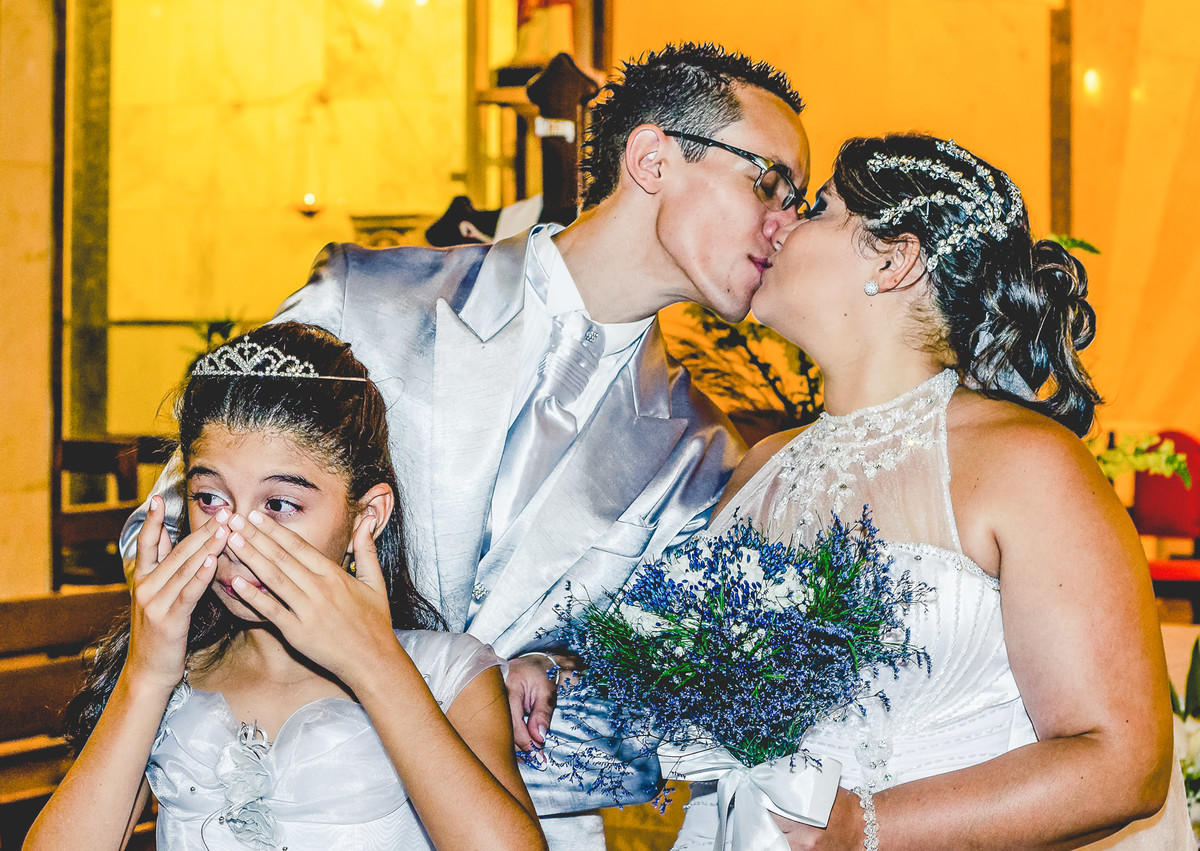 Fotografia dos noivos se beijando após a cerimônia de casamento e a daminha chorando na igreja Paróquia Nossa Senhora Aparecida em Mongaguá - Cia P&B - Fotografia 