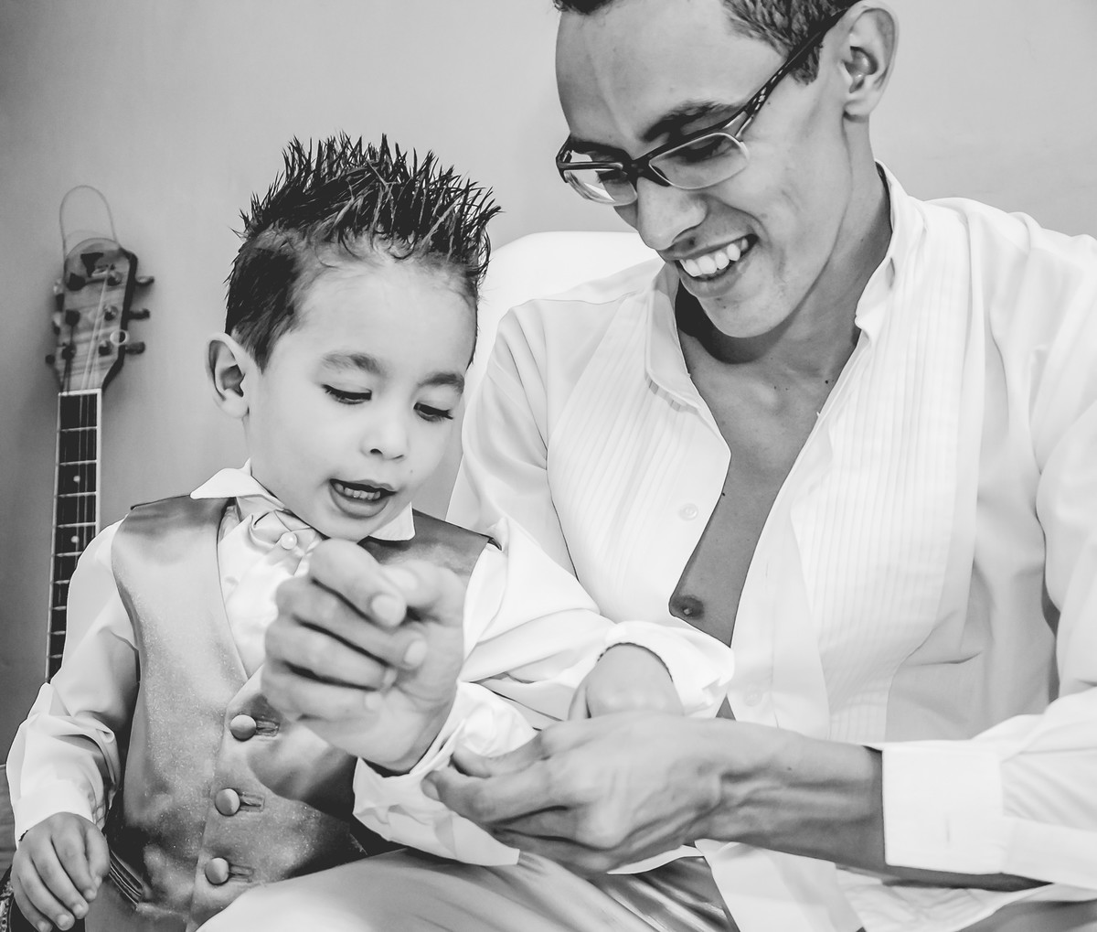 Fotografia do noivo com seu filho abotoando a manga da camisa durante o making of antes do casamento em Mongaguá - Cia P&B - Fotografia 