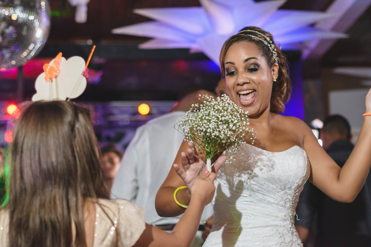 noiva Bethânia, recebendo o buquê da daminha, sorrindo, durante a festa, na cidade de Mongaguá - SP.
