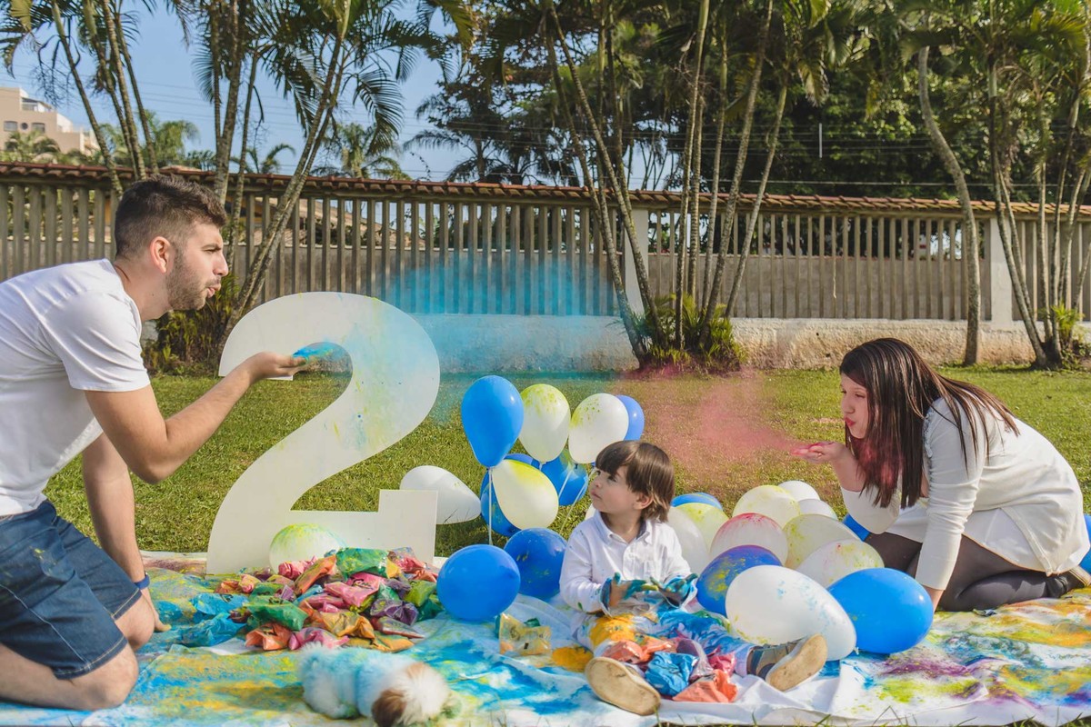 Foto do Enzo e seus pais brincando com as tintas em pó durante o ensaio infantil paint em Mongaguá - Cia P&B - Fotografia