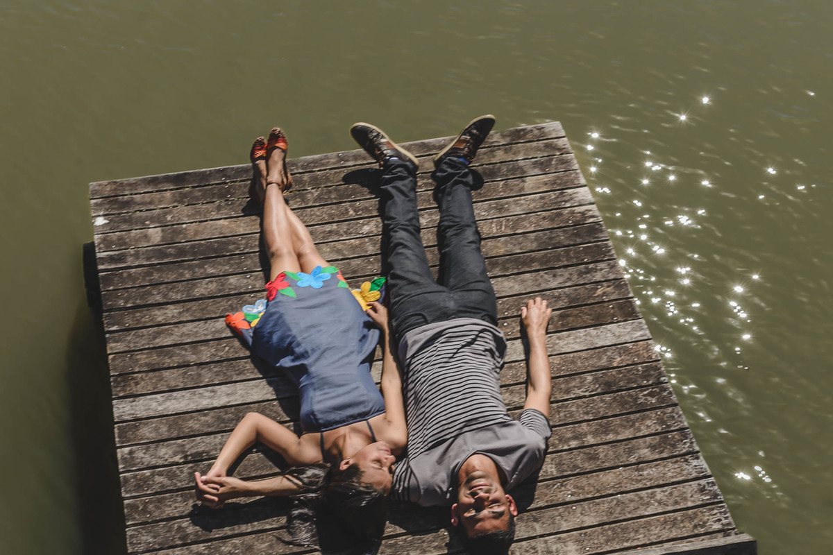 Foto dos Noivos deitados no trapiche sorrindo na  beira do lago no ensaio pré wedding no Parque tanguá - Curitiba - fotografia Cia P&B Produções 