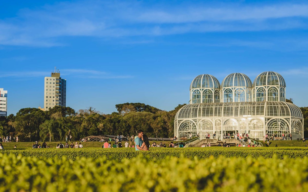 Foto dos Noivos abraçados no jardim francês com a estufa principal ao fundo no ensaio pré wedding - Jardim Botânico - Curitiba - fotografia Cia P&B Produções 