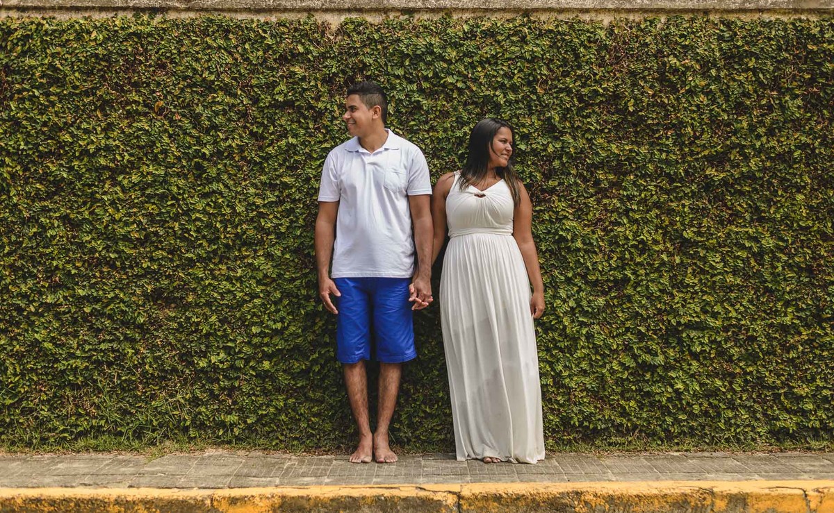 Foto dos Noivos de mãos dadas encostados em um muro de folhagens natural na praia dos Pescadores no ensaio pré wedding - Itanhaém - SP - fotografia Cia P&B Produções