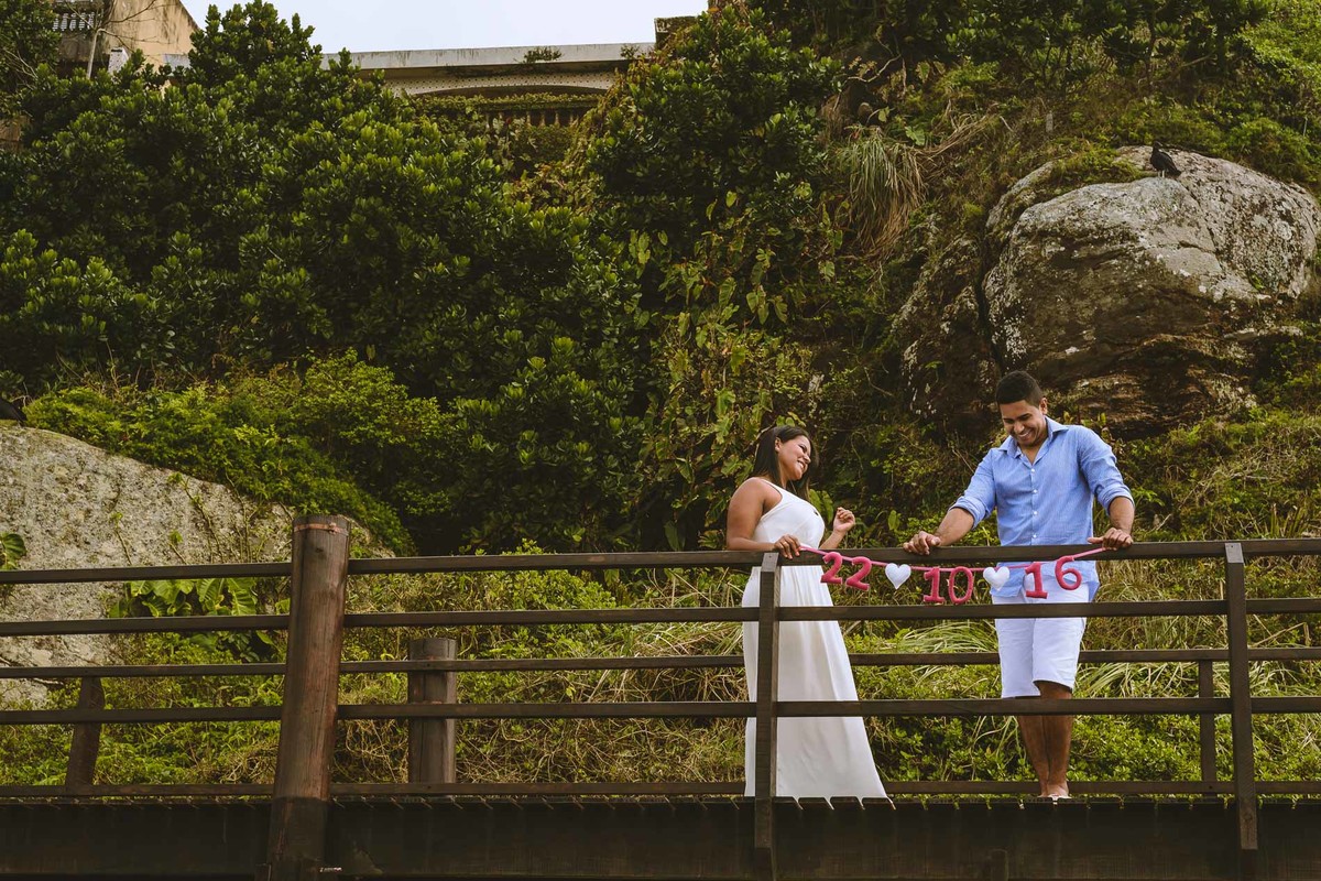 Foto dos Noivos na ponte com a faixa do save the date no ensaio pré wedding - Itanhaém - SP - fotografia Cia P&B Produções