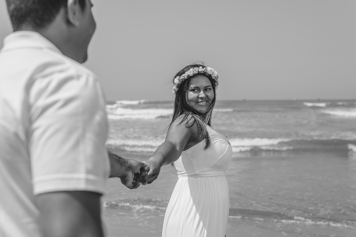 Foto dos noivos na praia de mãos dadas com a noiva olhando para o noivo - Praia dos Pescadores em Itanhaém - SP - Cia P&B Fotografia