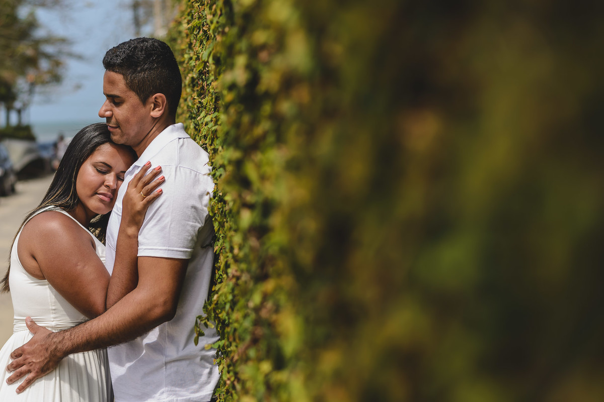 Foto dos Noivos abraçados de olhos fechados encostados em um muro de folhagens natural na praia dos Pescadores no ensaio pré wedding - Itanhaém - SP - fotografia Cia P&B Produções