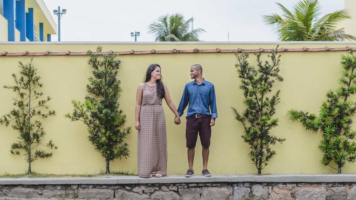 Foto dos noivos na parede amarela um de frente para o outro sorrindo - Itanhaém - SP - fotografia Cia P&B Produções 