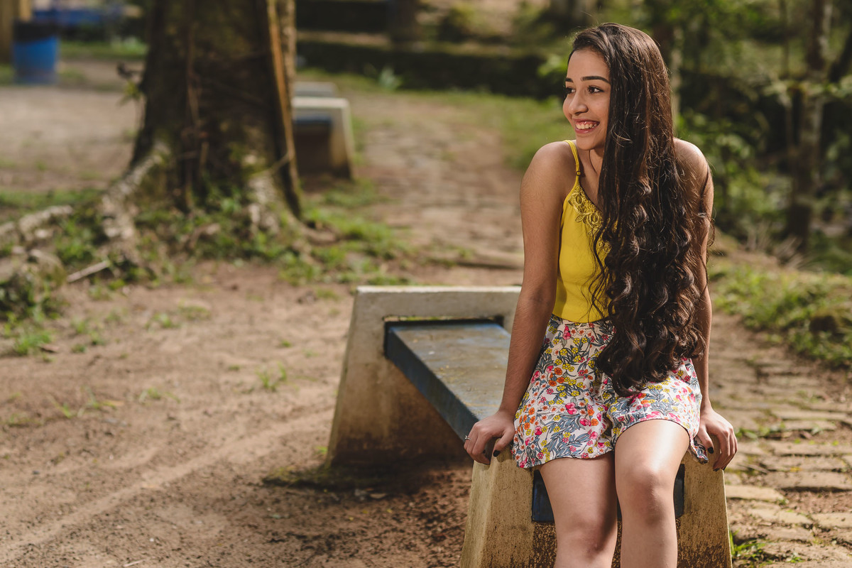 Ensaio de 15 anos debutante sorrindo, sentada no banco admirando a natureza do local - Poço das Antas - Mongaguá - SP - fotografia Cia P&B