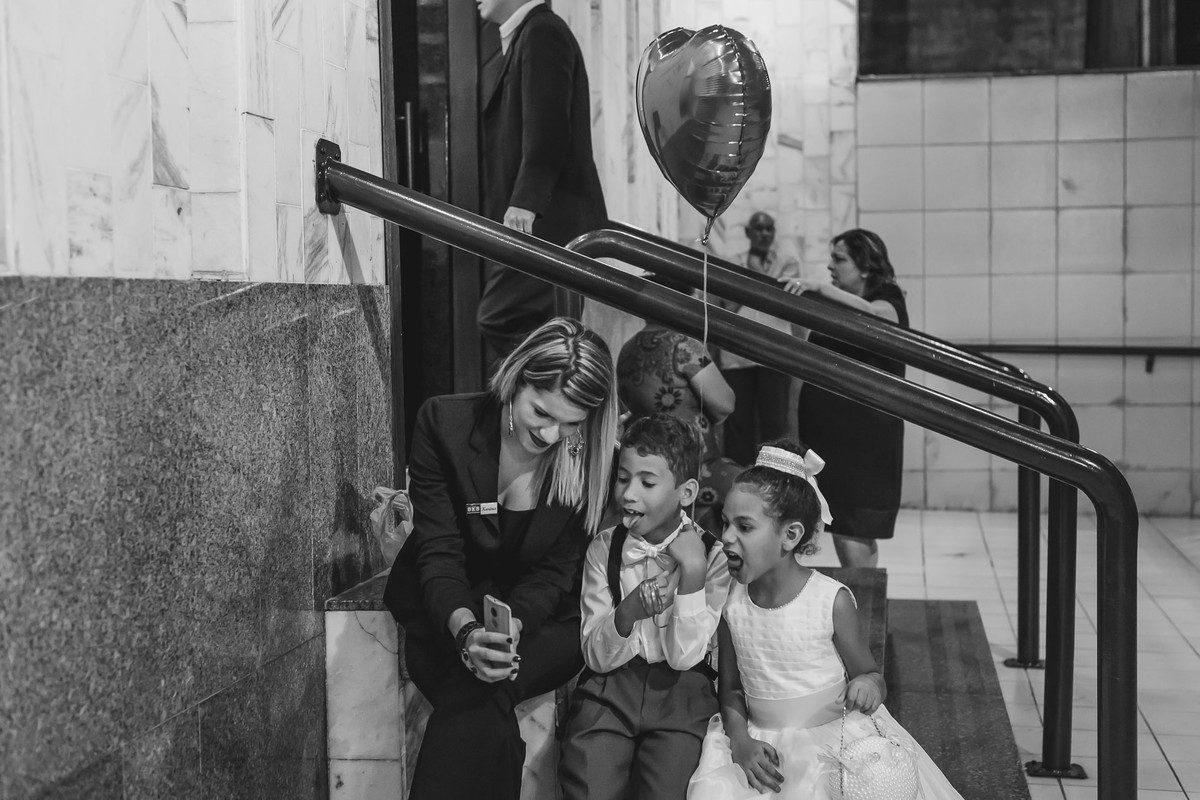 Foto do pagem e daminha com balão de coração antes de entrarem na igreja vendo o celular da assessora em Praia Grande - SP - fotografia Cia P&B Produções 