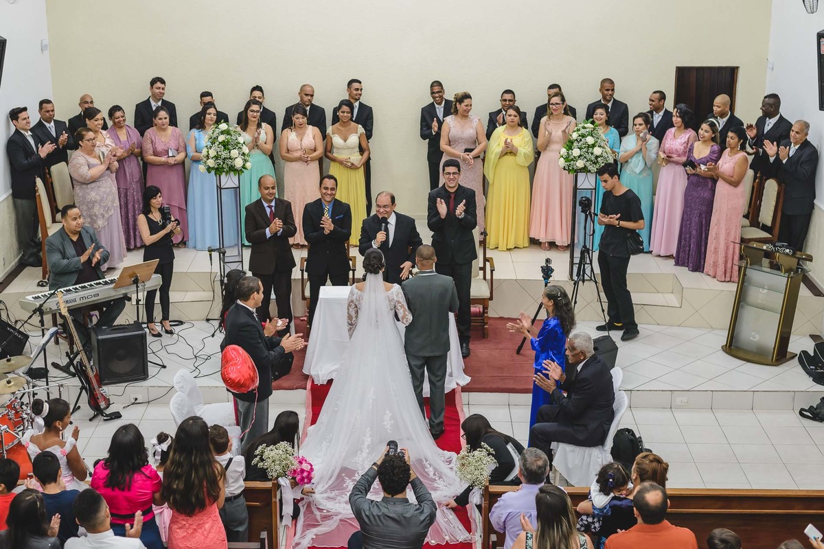 Foto panorâmica dos noivos recendo a benção do pastor e aplausos dos pais, padrinhos e convidados na cerimônia de casamento em Praia Grande - SP - fotografia Cia P&B Produções 