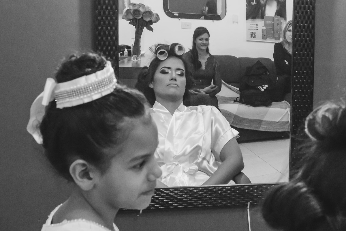 Foto da irmã da noiva olhando para ela com o reflexo da mãe delas no espelho no making of em Praia Grande - SP - fotografia Cia P&B Produções 