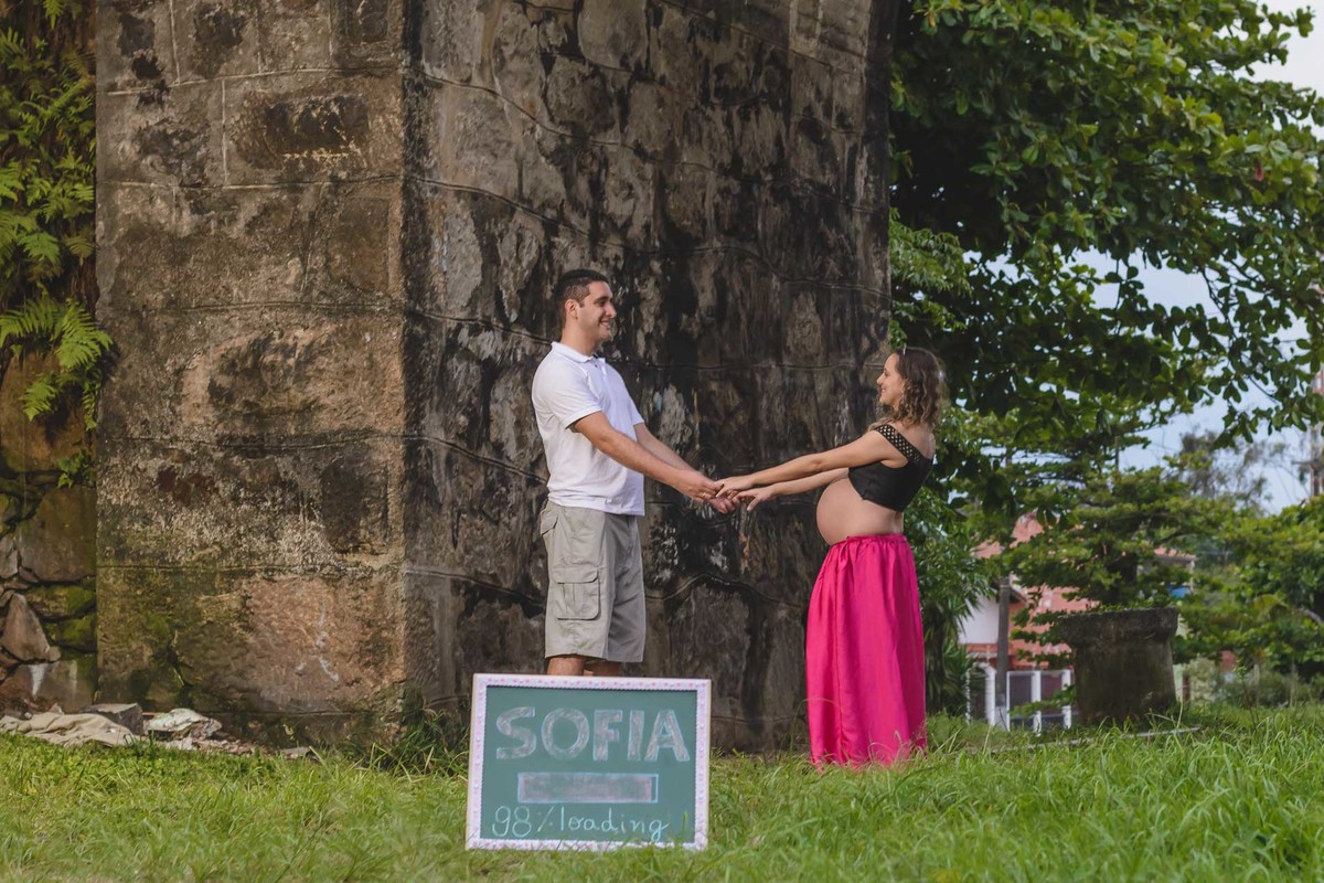 foto da gestante e do marido dando as mãos com  lousa. Ensaio de gestante feito pela Cia P&B Produções Itanhaém - SP