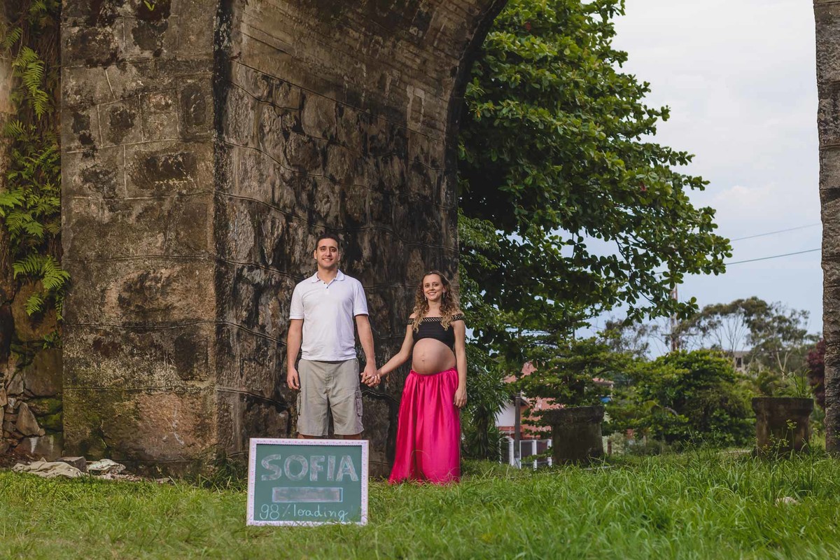 foto da gestante e do marido dando as mãos embaixo de um arco. Ensaio de gestante feito pela Cia P&B Produções Itanhaém - SP