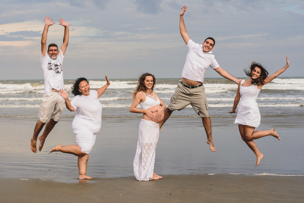 Foto da gestante com a família pulando na praia. Ensaio de gestante feito pela Cia P&B Produções Itanhaém - SP