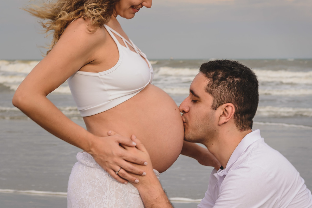 foto do marido beijando a barriga da gestante na praia. Ensaio de gestante feito pela Cia P&B Produções Itanhaém - SP