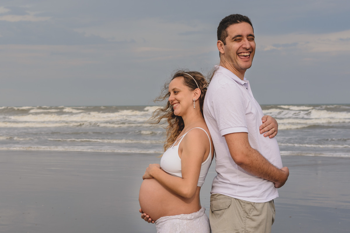 Foto da gestante e do marido na praia brincando. Ensaio de gestante feito pela Cia P&B Produções Itanhaém - SP