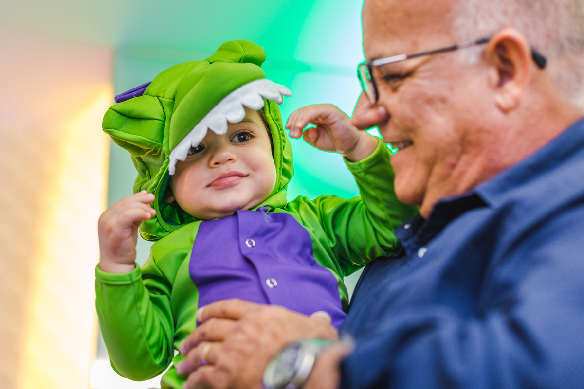 bebê vestido com roupa de dinossauro no colo do avô