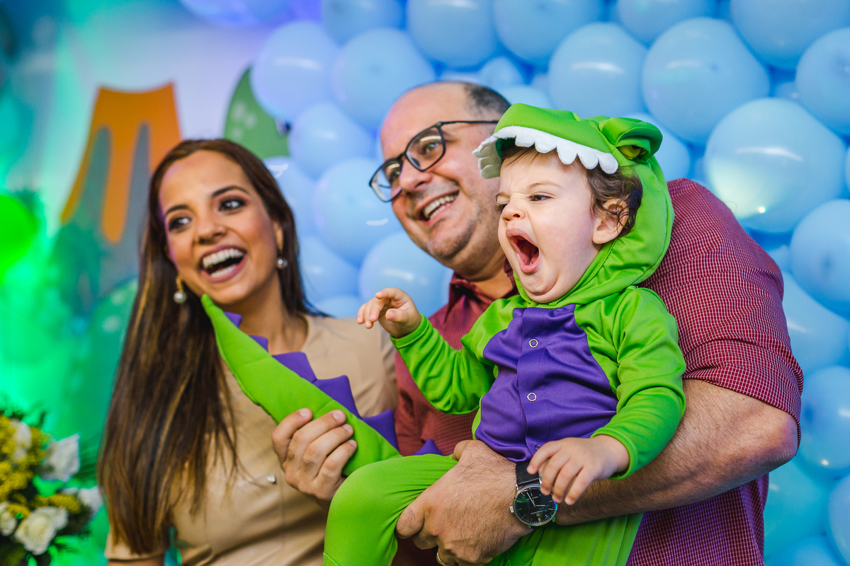 bebê bocejando e o pai segurando a cauda da roupa de dinossauro