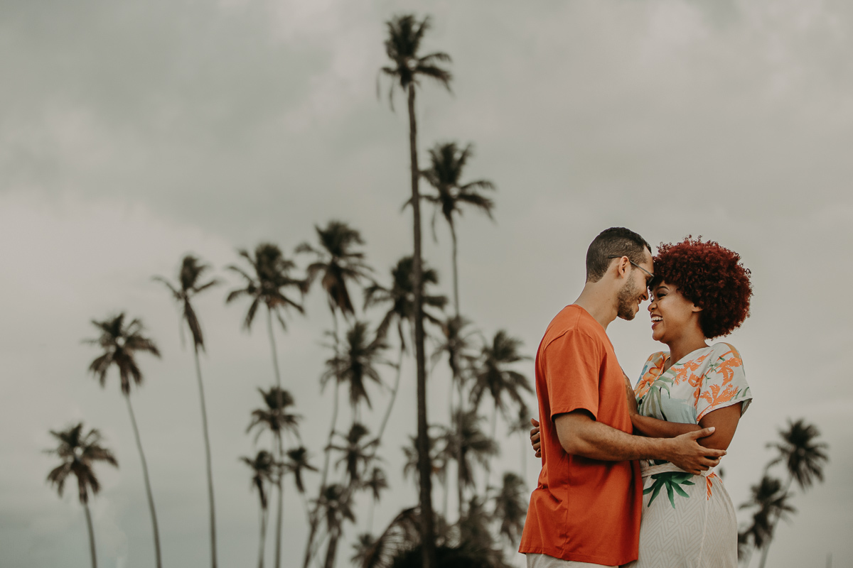 casal rindo e abraçados. Ao fundo os coqueiros da praia