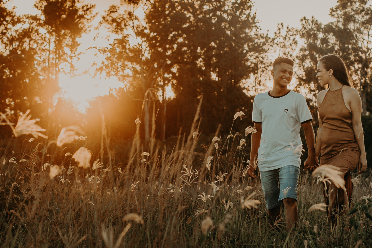noivos caminhando na vegetação e o por do sol ao fundo