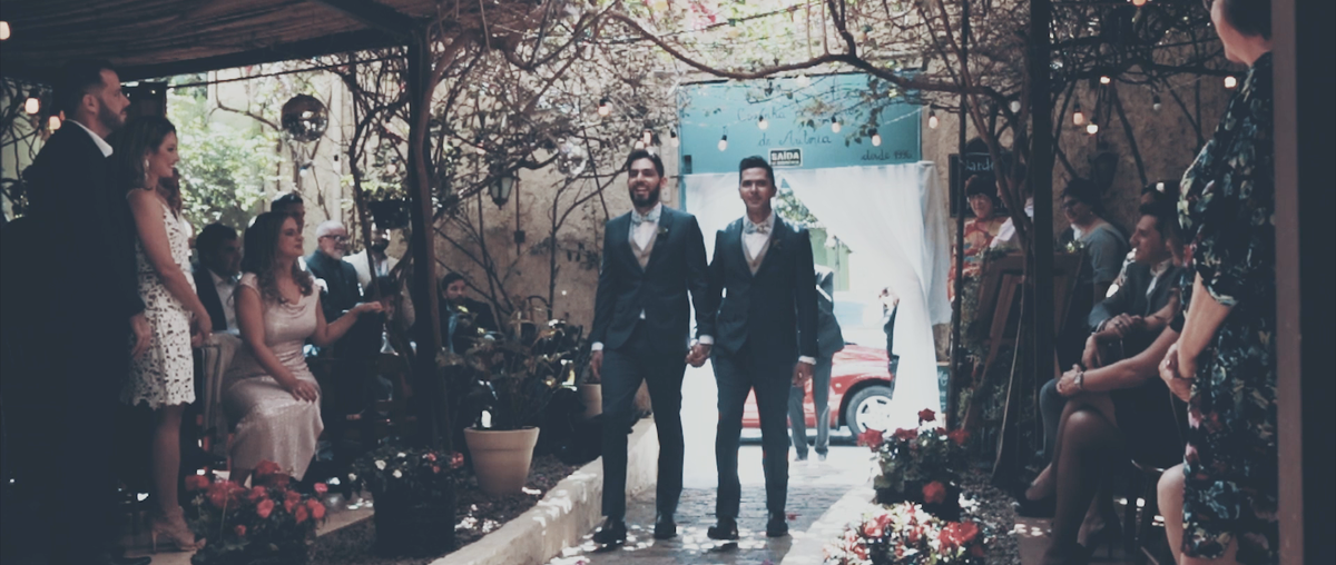 As pessoas celebram de pé a entrada de Elry e Gauss. O primeiro casamento igualitário produzido pela Gravata Florida Filmes. O casamento aconteceu no Ruella Bistrô, em São Paulo.