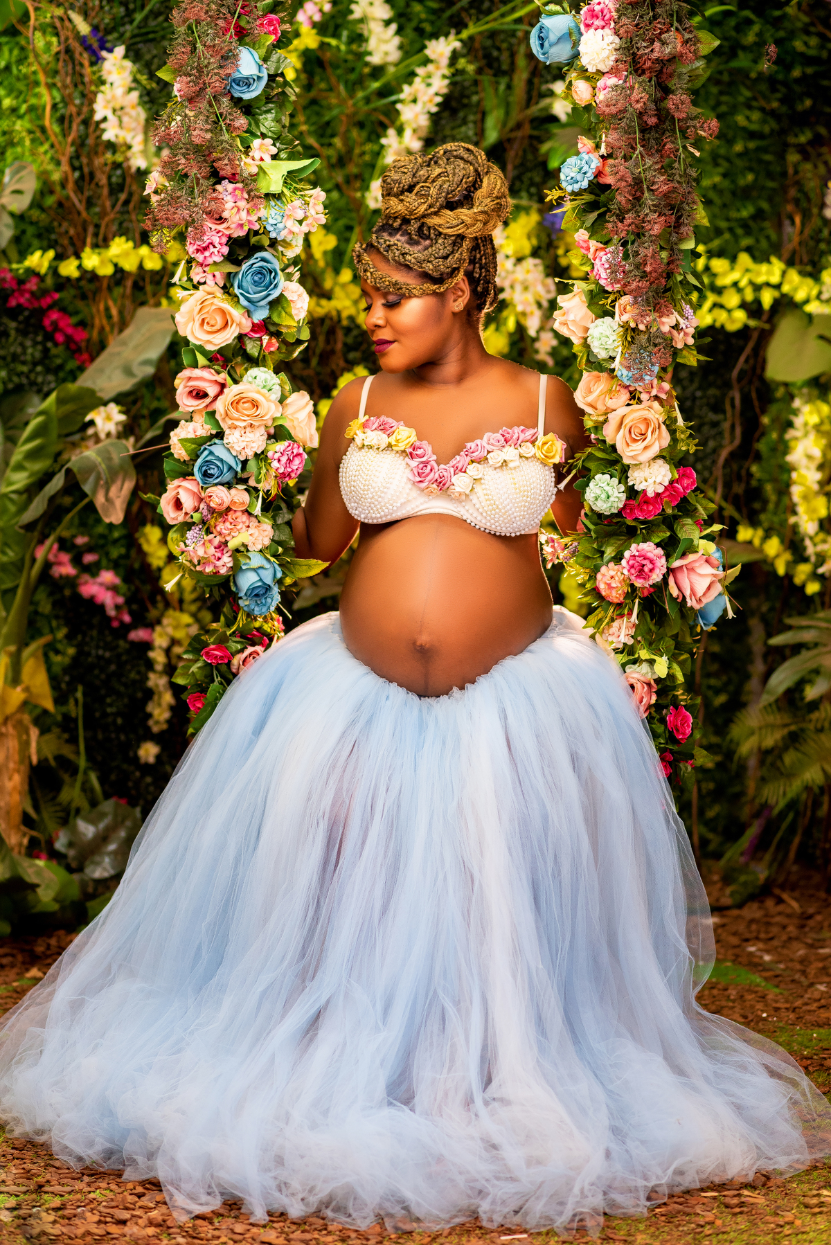 Foto 1: No aconchego do jardim, Larissa Lacerda e seu esposo Shalom compartilham um momento especial enquanto esperam a chegada do seu bebê. Vestida em um elegante e imaculado vestido branco, Larissa irradia serenidade e beleza materna. 