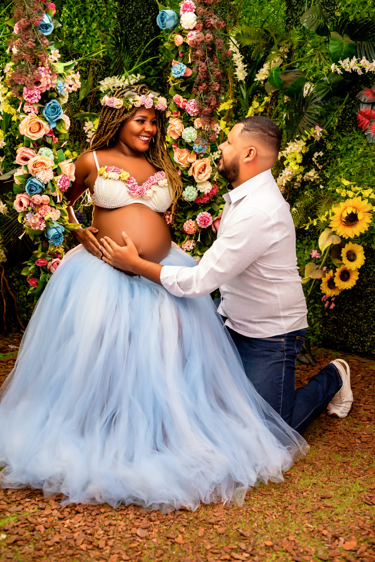 No aconchego do jardim, Larissa Lacerda e Shalom compartilham um momento íntimo, envolvidos na doce espera pelo seu bebê. Larissa deslumbra em seu vestido branco, emanando uma elegância serena.