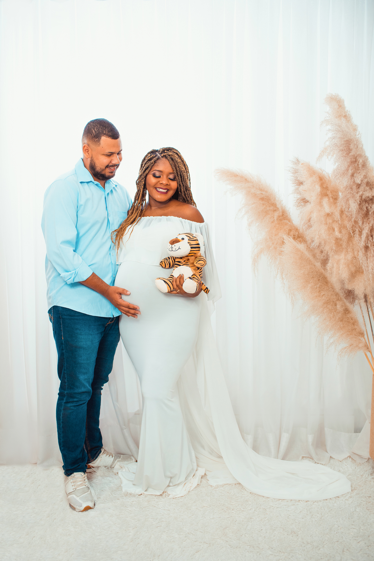 Larissa e Shalom são retratados no cenário clean, onde a simplicidade encontra a elegância. Vestida em um deslumbrante vestido branco, Larissa irradia uma energia suave e maternal. 