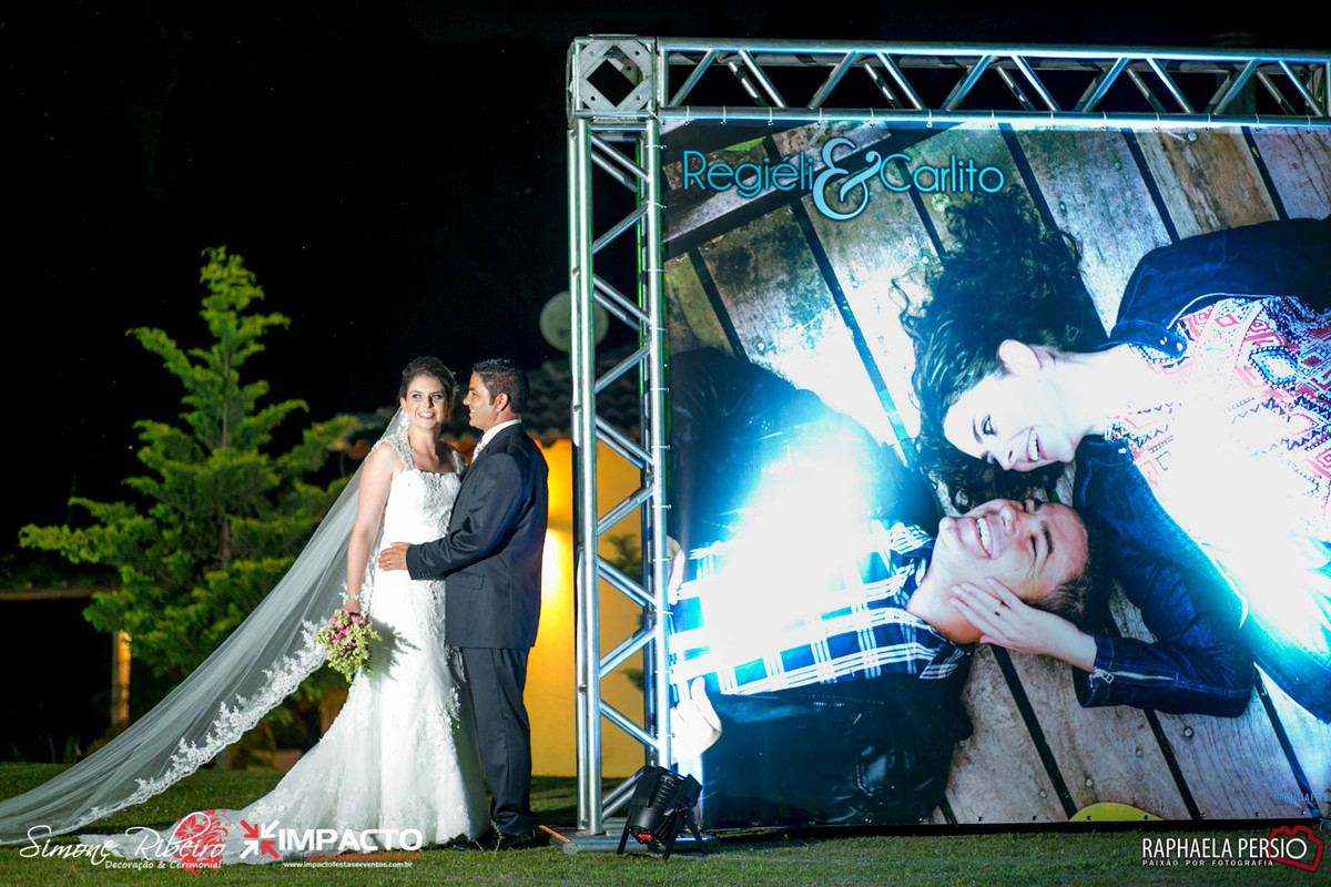 noivos sorrindo ao lado de banner grande