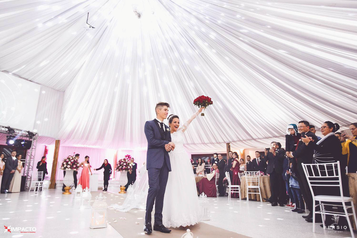 Noivos entrando no salão, noiva segura o buquês no alto