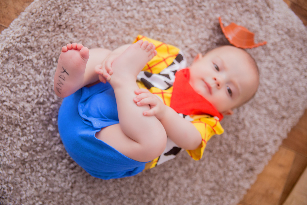 o pé do bebê aparece enquanto ele está deitado no cenário de toy story em sua sessão de acompanhamento mensal