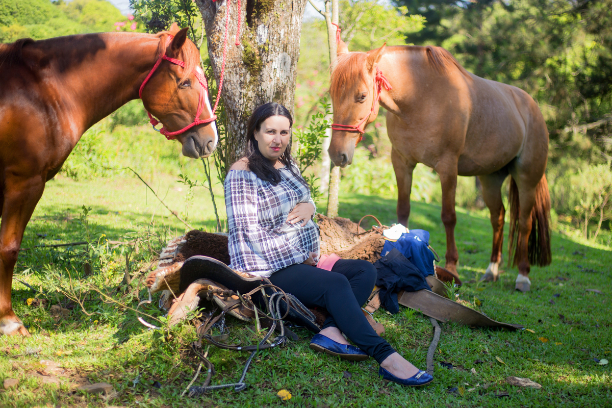 a gestante senta próximo aos cavalos em sua sessão de grávida
