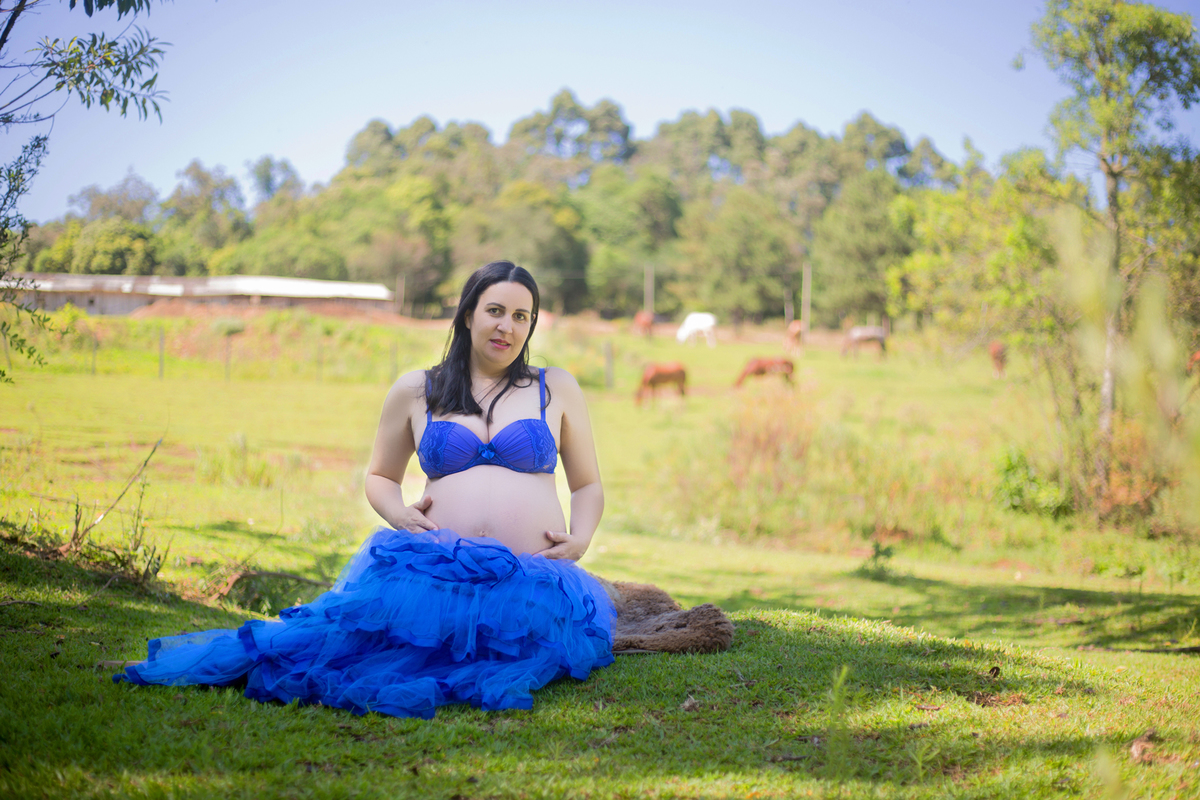 a gestante está sentada no chão, posando para a fotógrafa em sua sessão de fotos