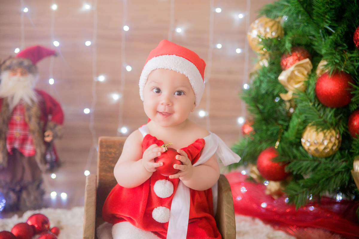a bolinha de natal está na mão da bebê em sua sessão de fotos infantis
