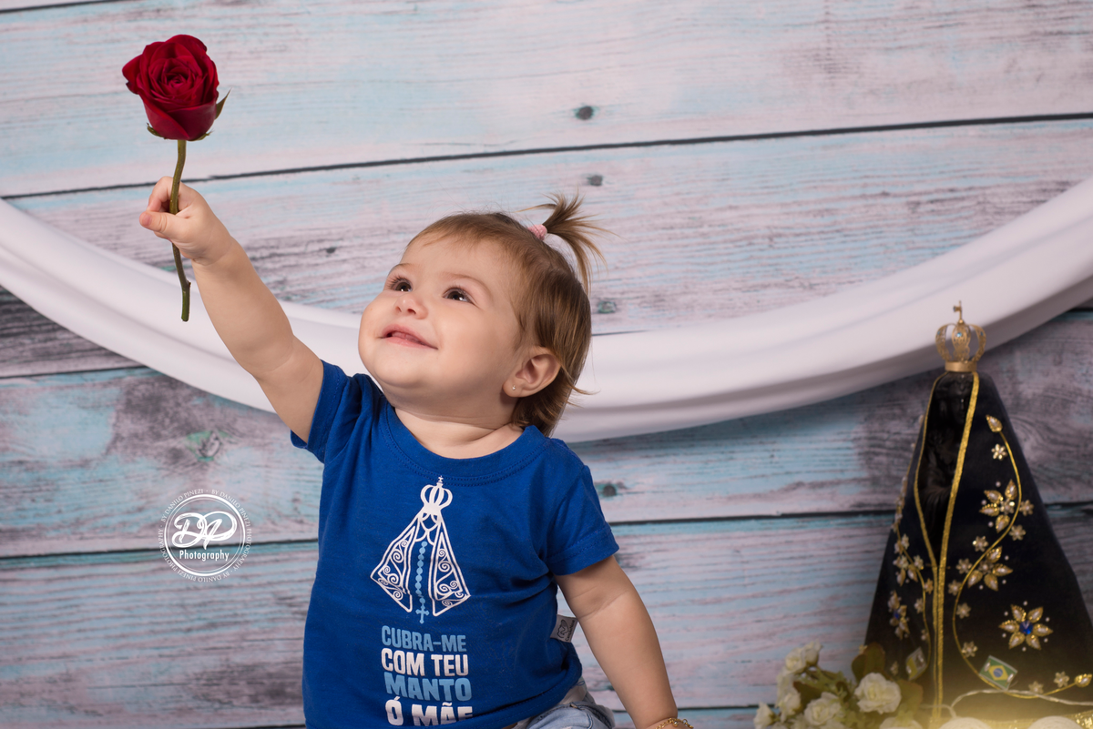 Sessão de um ano de menina, em homenagem à Nossa Senhora Aparecida, com camisetas personalizadas, imagem, luzes e rosa vermelha