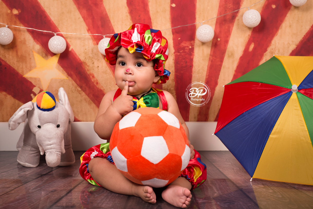 Bebê vestido de palhaço de circo, brincando em meio a brinquedos do tema, em sessão feita no estúdio Danilo Pnezi Fotografia em Bariri