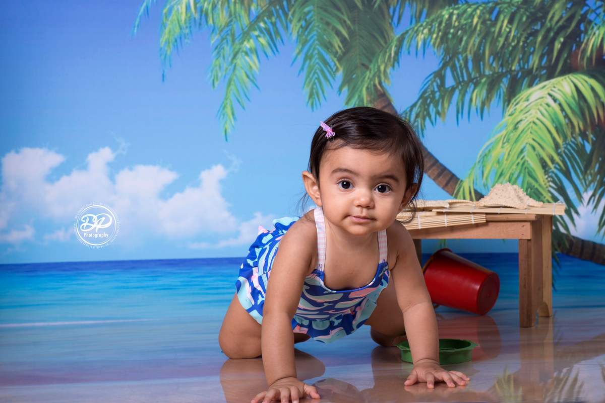 Sessão fotográfica de bebê menina na praia, com óculos e espreguiçadeira