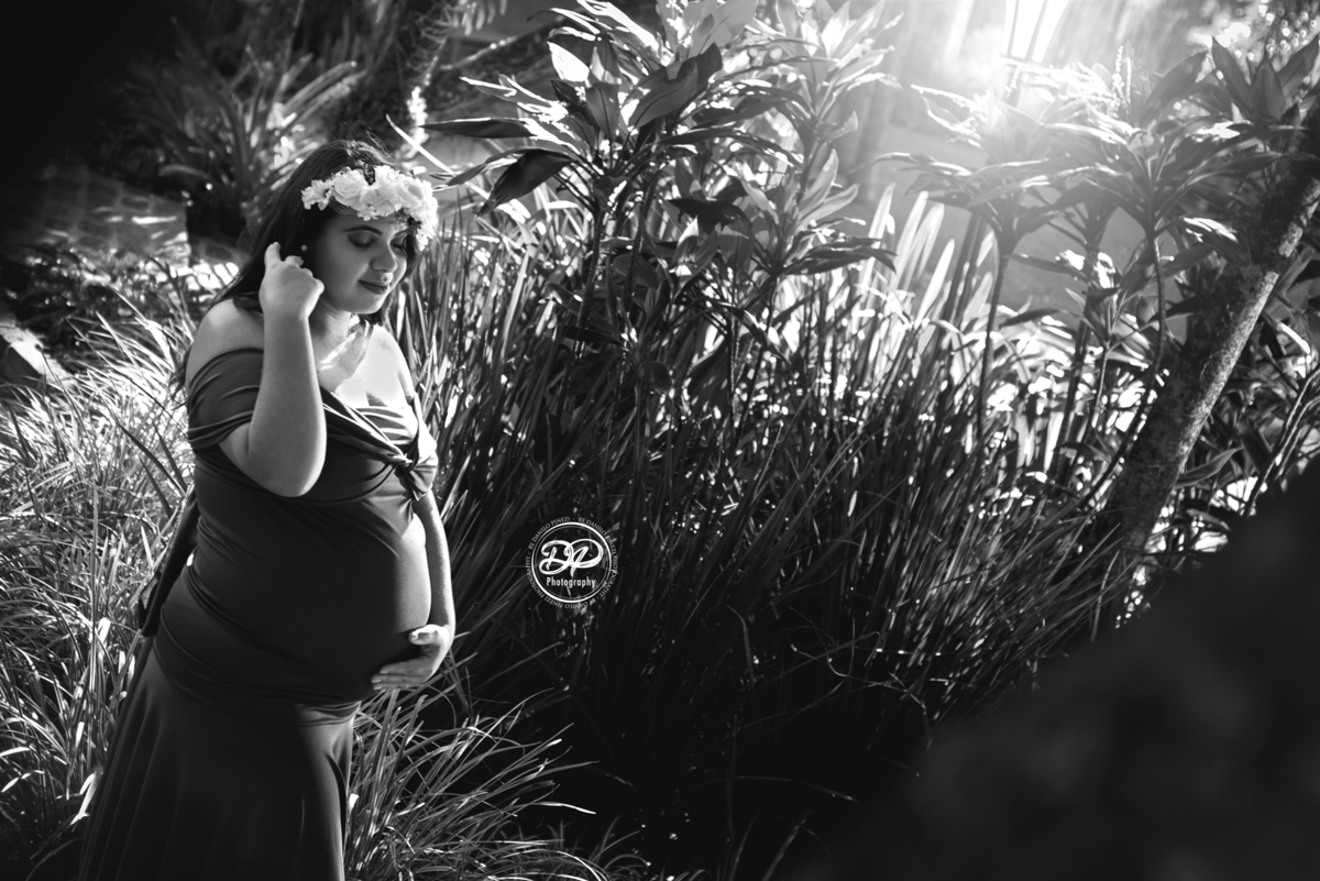 gestante com vestido roxo em pé, de perfil com uma das mãos na barriga e a outra arrumando o cabelo,  Fotografia gestante em preto e branco