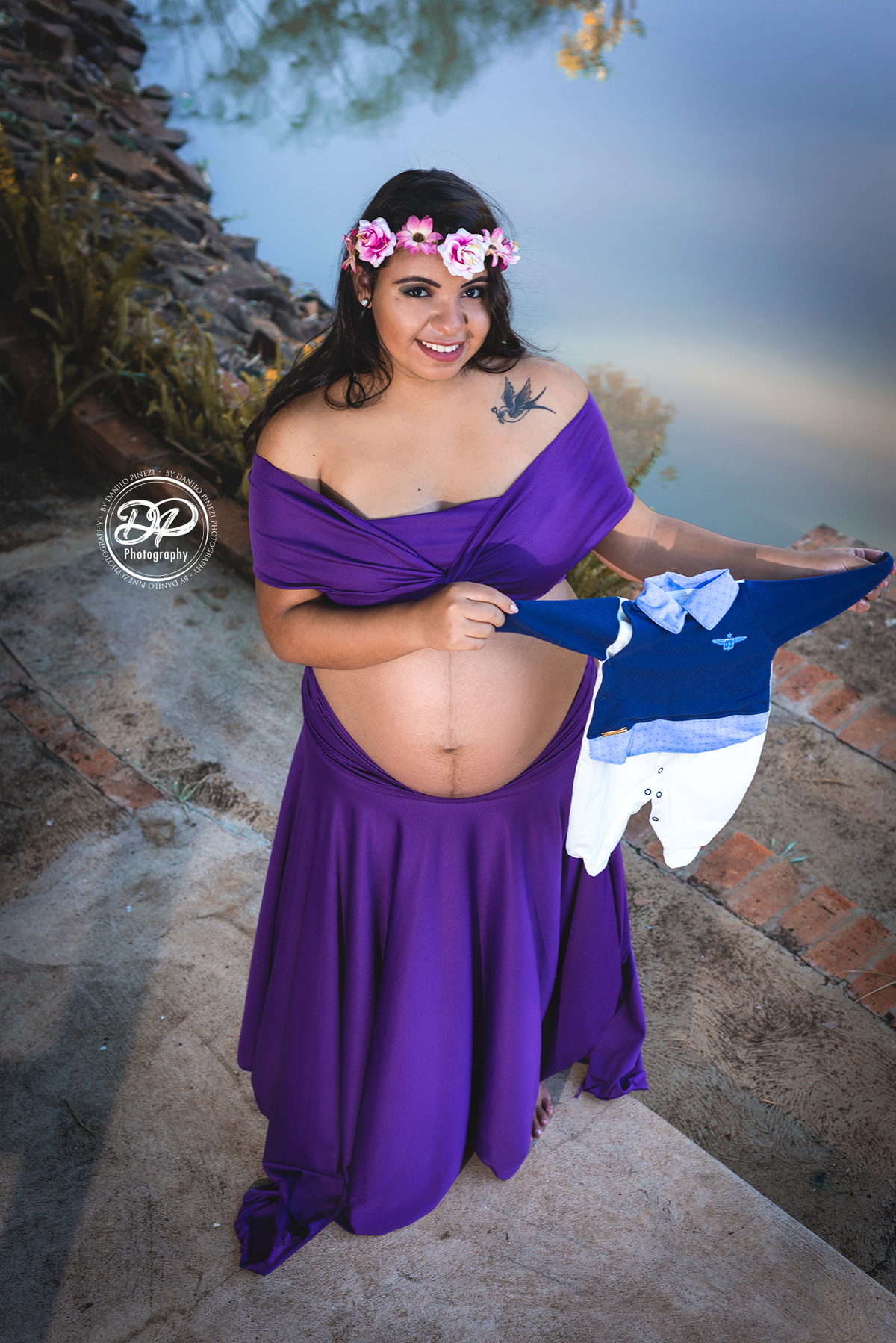 Gestante com vestido roxo, em pé segurando a roupinha de seu bebê