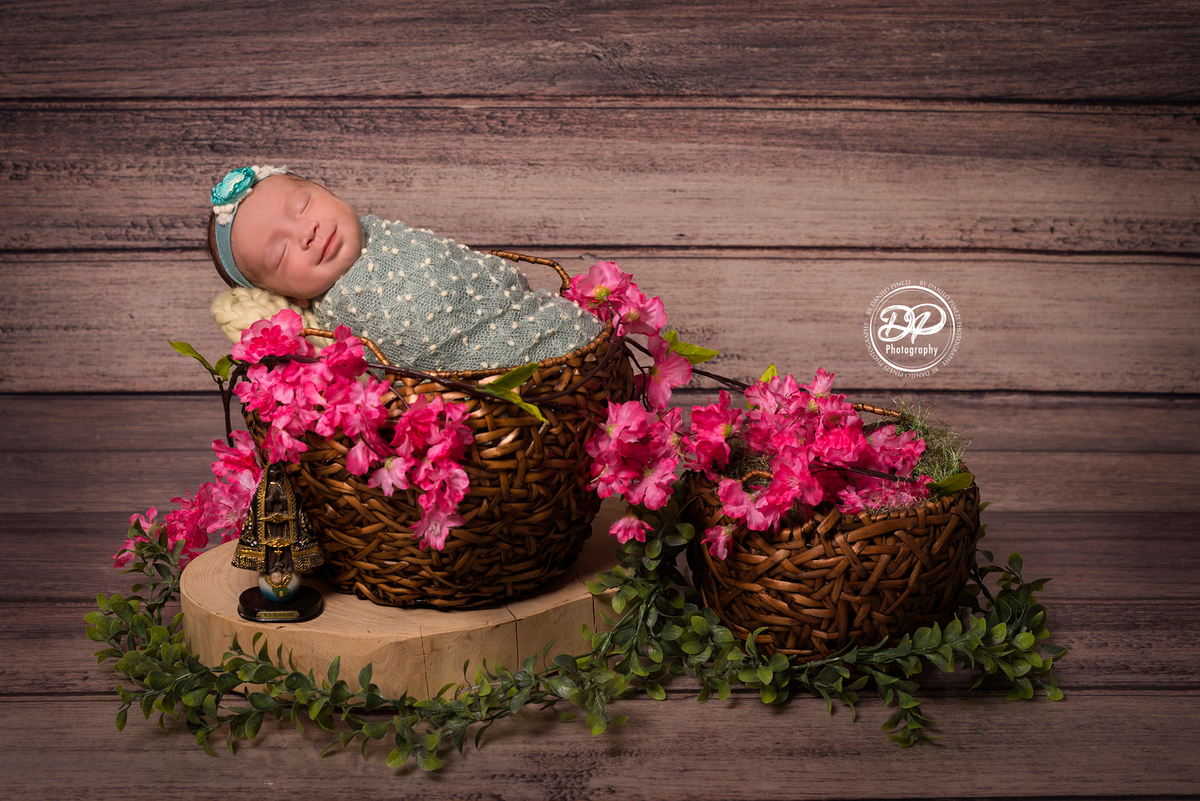 Bebê recém nascida sorrindo, dormindo tranquilamente enrolada em wrap pipoca, dentro de um cesto enfeitado com cerejeiras,  em sessão newborn realizada no Estúdio Danilo Pinezi Fotografia em Bariri